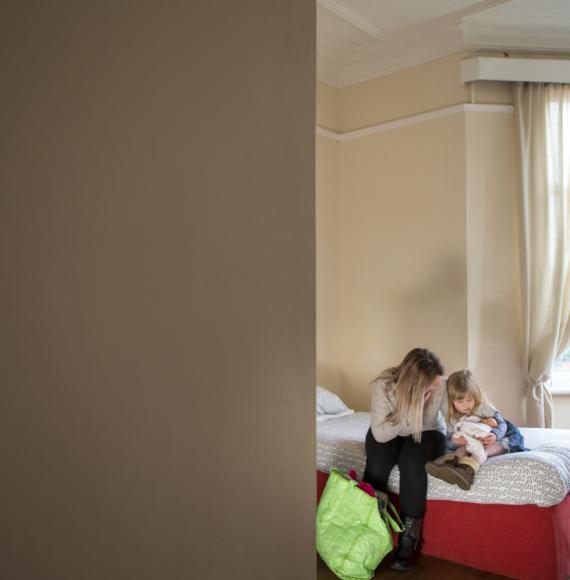 A young mother and daughter sit on a bed in a dingy woman's support centre