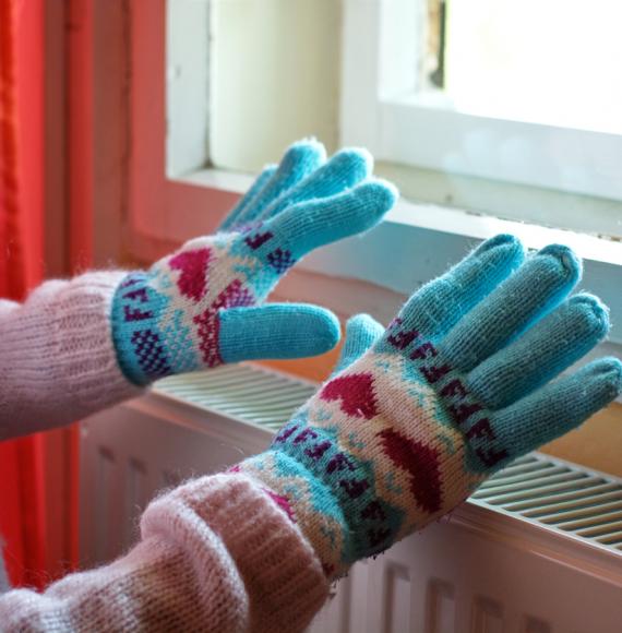 Woman heating gloved hands on raditator