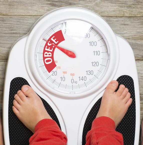 Child standing on scales pointing to 'obese'