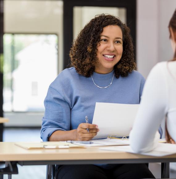 The office manager holds onto a resume while speaking with the new intern they are considering.