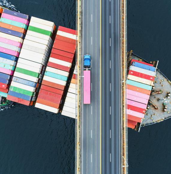 Big freight ship passing under a road bridge with a truck on it