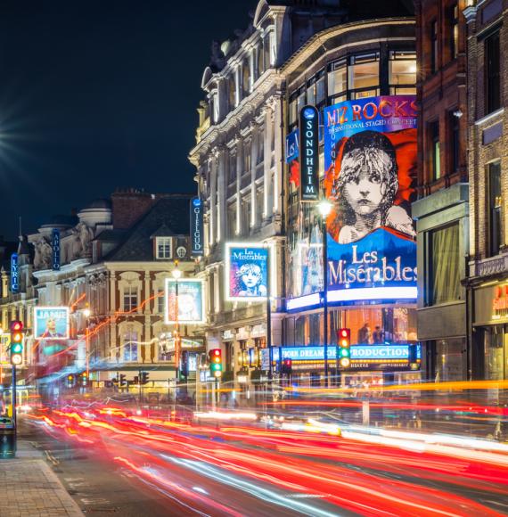 Traffic zooming along Shaftesbury Avenue past the tourist crowds and the billboards of London’s vibrant theatre district at night.