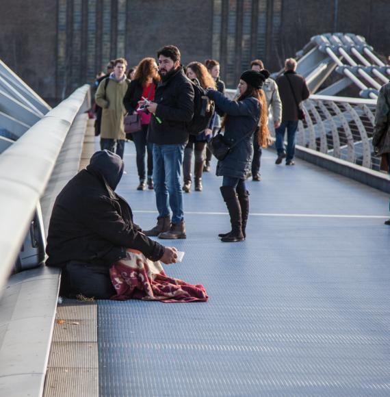 Homeless person surrounded by tourists on a bridge in London