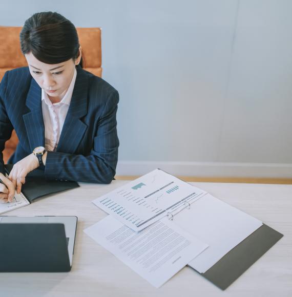 Woman working on a laptop with papers on the desk in front of her