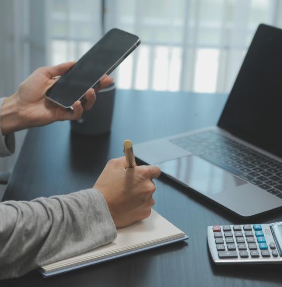 Person working on phone and laptop with a notepad and calculator