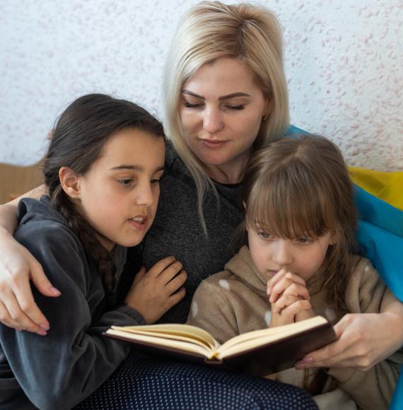 Mother and daughter reading a book with the flag of ukraine in bed