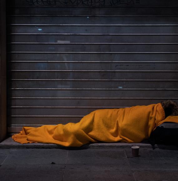 A homeless person sleeps on the street under a blanket