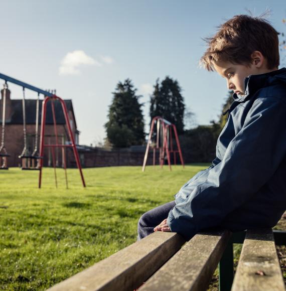 Lonely child sitting on play park playground bench