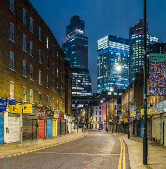 The futuristic towers of the City financial district illuminated at night overlooking the quiet streets and shops of Petticoat Lane Market in Spitafields, London