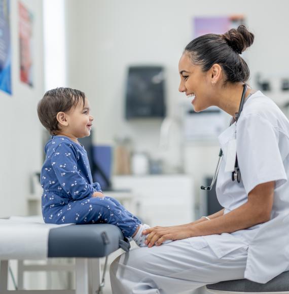 A sweet little toddler sits up on an exam table in a doctors office as her female doctor conducts a routine check-up.