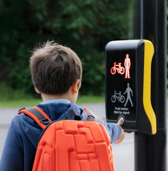 School kid pressing a button at traffic lights on pedestrian crossing on way to school