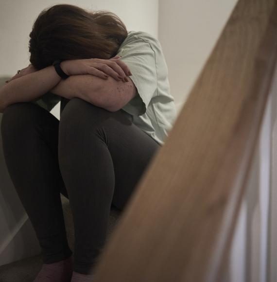 A woman suffering from depression or domestic abuse sat on the stairs of her home hiding her face.