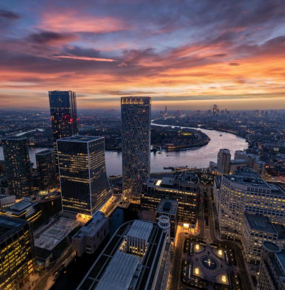 Panoramic view through the modern skyscrapers of Canary Wharf of the illuminated London skyline and Thames river during dusk time, England