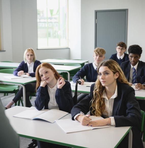 Front view of secondary students wearing uniforms and sitting side by side at desks