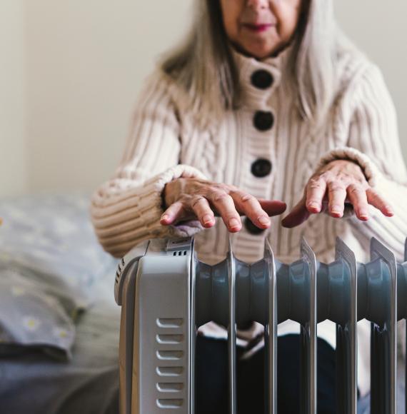 A pensioner sits in her cold home, next to a space heater