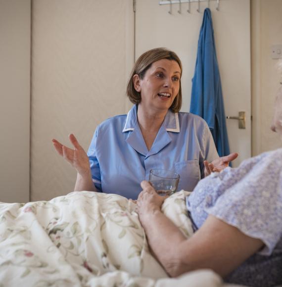 Senior woman lying in bed being helped by a home carer