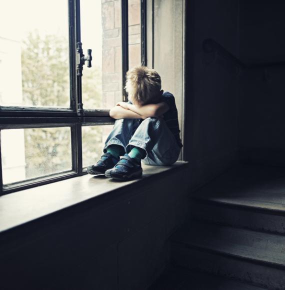 Depressed child sitting on window